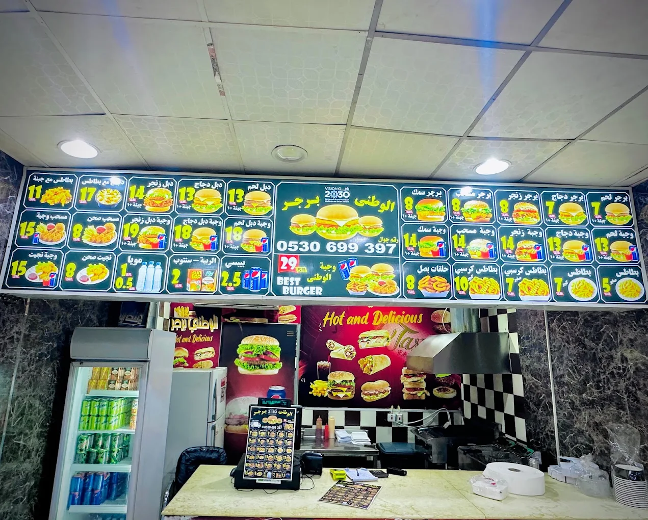 Al Watani Burger counter in Jeddah with the illuminated menu board above it